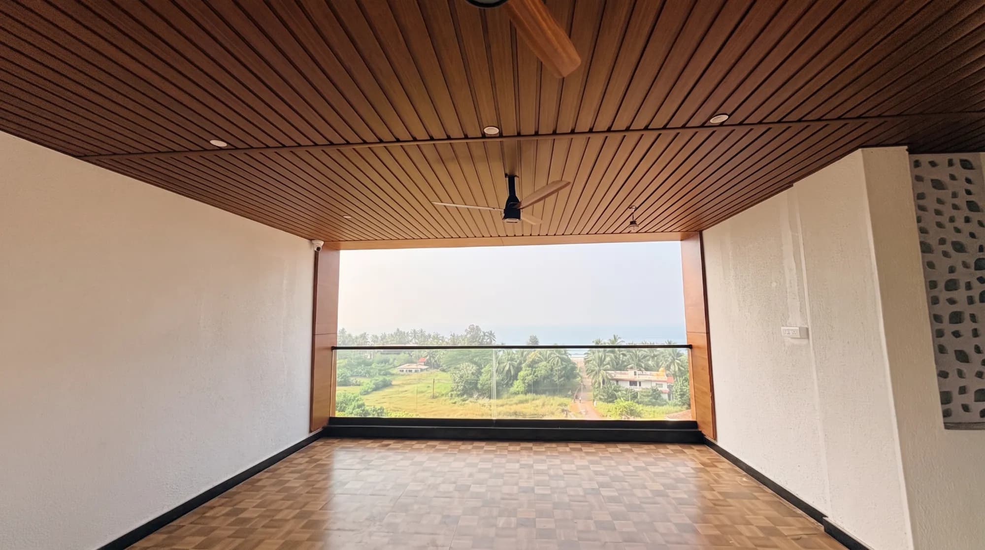 An open upper-floor space under a wooden ceiling, looking over coconut palms to the sea